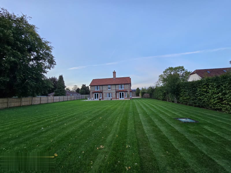 Country house at golden hour — wide view of the rear garden with manicured lawn leading to the brick and flint elevations