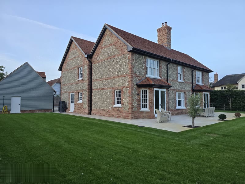 Side angle showing the mixed flint and brick walls, sash windows and paved patio